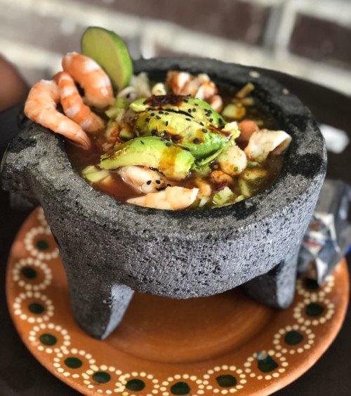 cóctel de camarón servido en un molcajete, adornado con rodajas de limón, perejil fresco y trozos de aguacate.